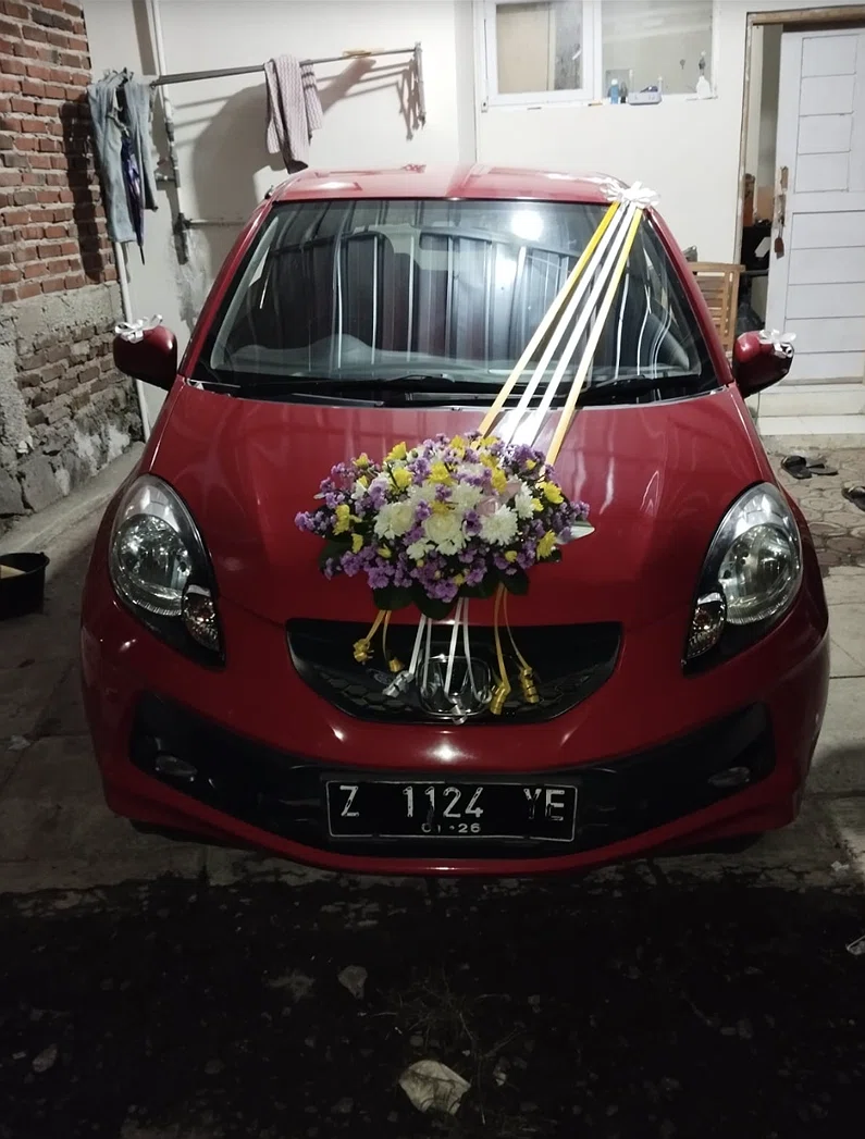 Bunga Mobil Pernikahan Tasikmalaya (mobil merah dengan rangkaian bunga putih kuning ungu dan pita)